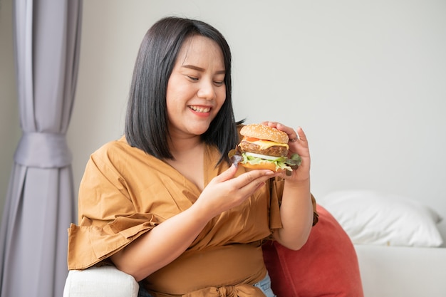kobieta uśmiecha się i trzyma hamburgera i siedzi w salonie