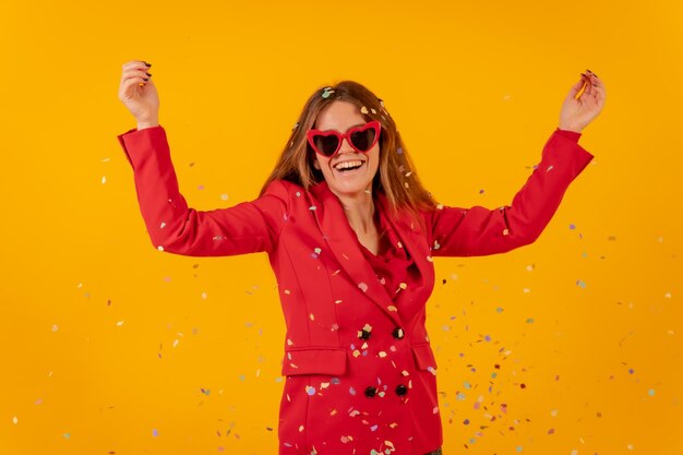 Kobieta uśmiechająca się w czerwonej sukience na żółtym tle rzucająca konfetti z koncepcją strony
