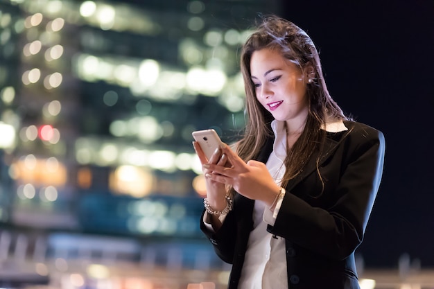 Kobieta używa jej smatphone plenerowego w wieczór w nowożytnym miasta położeniu