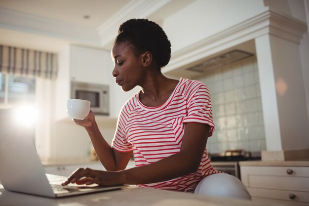 Kobieta używa laptop podczas gdy mieć kawę w kuchni