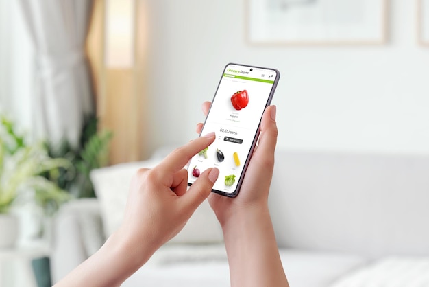 Kobieta używa smartfona do kupowania artykułów spożywczych Dodaj czerwoną paprykę do koszyka koncepcja online Inteligentny telefon w rękach kobiety Wnętrze domu w tle