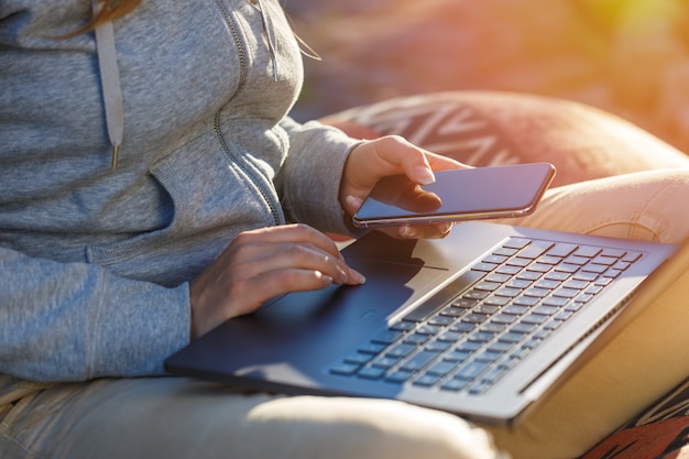 Zdjęcie kobieta używa smartfona i laptopa na zewnątrz. tło z blaskiem słońca jest niewyraźne.