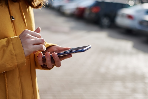 Kobieta używa smartphone w mieście plenerowym, zamyka up. Kobieta ręce pisania wiadomości na telefon komórkowy