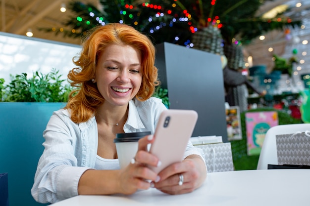 Kobieta używa telefon komórkowego podczas gdy pijący kawę przy zakupy centrum handlowym