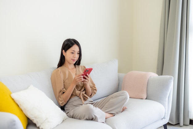 Kobieta używa telefonu komórkowego i siedzi na kanapie w domu