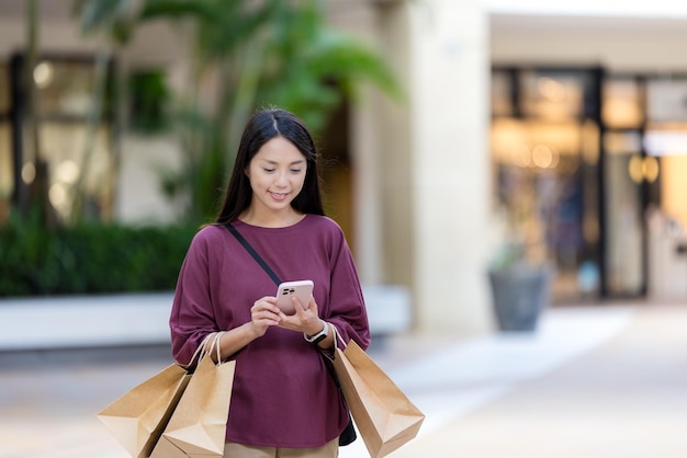 Kobieta używa telefonu komórkowego z torbą na zakupy na placu