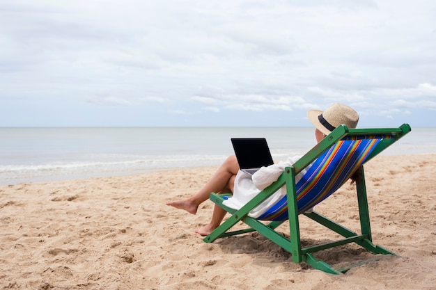 Kobieta używająca laptopa i pisząca na nim podczas leżenia na leżaku