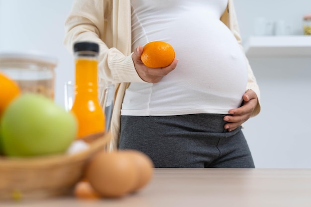 Kobieta w 28 tygodniu ciąży trzyma pomarańczę i wybiera pożywną dietę dla zdrowego rozwoju i wzrostu jej nienarodzonego dziecka