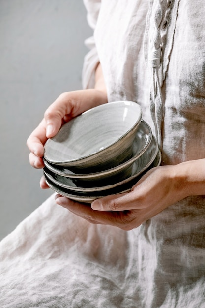 Kobieta w bawełnianej sukience trzymaj w rękach zestaw pustych ceramicznych misek wykonanych z szarej glazury