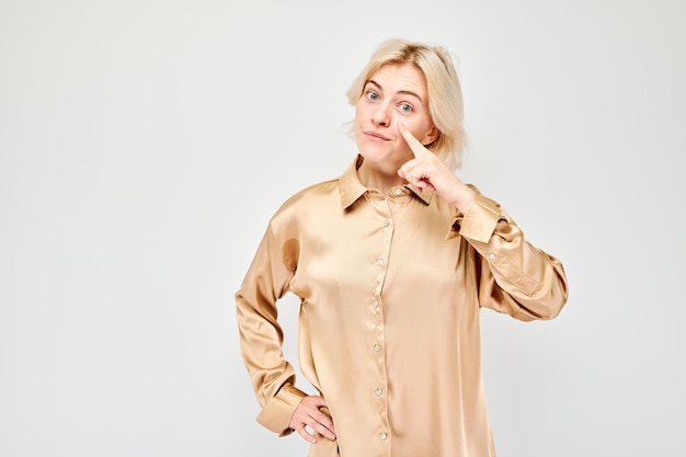 Kobieta w beżowej bluzce rozmyśla z ręką na twarzy izolowana na jasnym tle