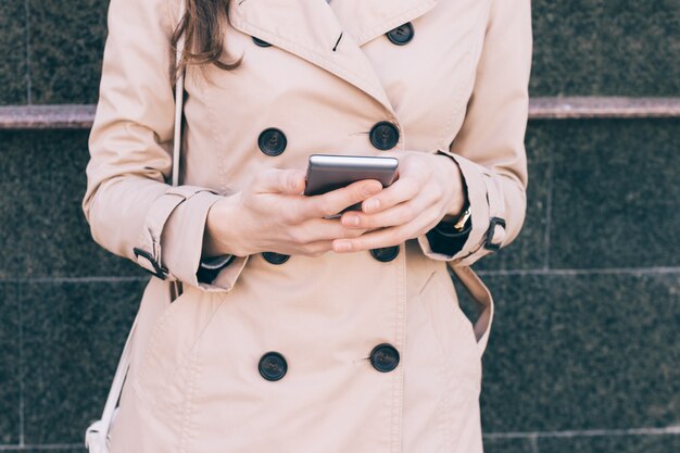 Kobieta W Beżowym Płaszczu Trzyma W Rękach Telefon Komórkowy