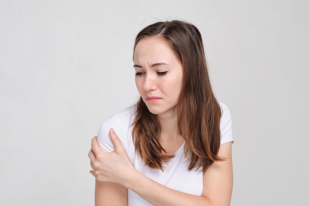 Kobieta w białej koszulce smaruje ramię ręką. Pojęcie bólu mięśni.