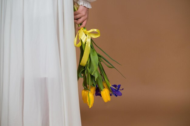 Kobieta w białej sukni trzyma bukiet tulipanów i irysów zbliżenie 8 marca Dzień Kobiet Święto Kobiet Święto Mamy Bukiet kwiatów