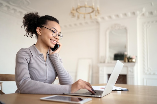 Kobieta w biurze w okularach pracuje na laptopie, odbiera maile i telefony klientów