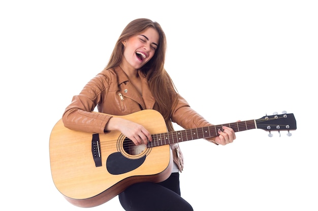Kobieta w brązowej kurtce i czarnych spodniach grająca na gitarze na białym tle w studio