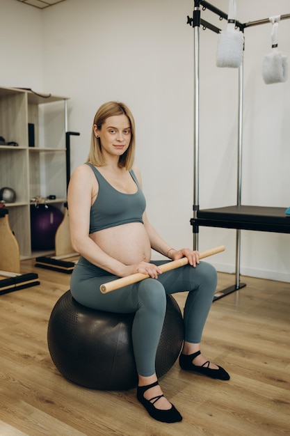 Kobieta w ciąży ćwicząca z pomocą reformatora na zajęciach pilates