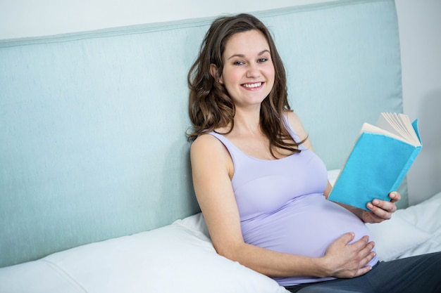 Kobieta w ciąży czyta książkę kłama na jej łóżku