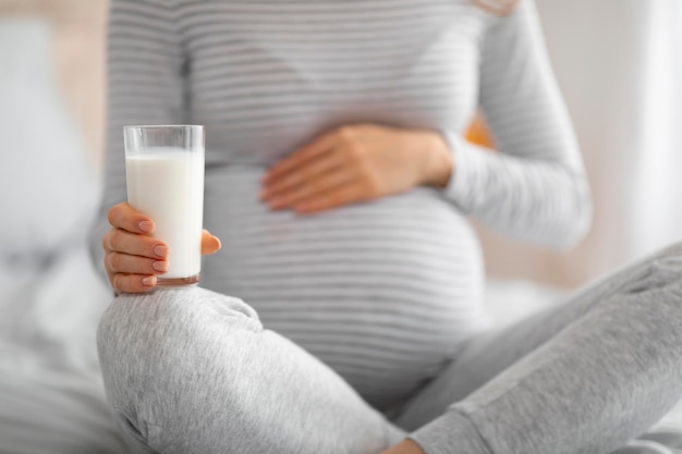 Kobieta w ciąży delikatnie trzyma szklankę mleka