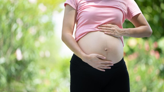 Kobieta w ciąży dotykająca brzucha w parku miejskim Ciąża Relaks i ćwiczenia Piękny, czuły nastrój zdjęcie ciąży