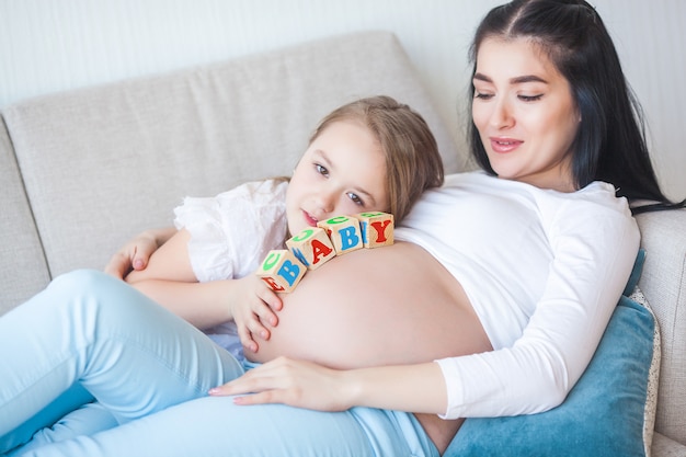 Kobieta w ciąży i jej córeczka zabawy w pomieszczeniu. Macierzyństwo. Młoda matka czeka na narodziny dziecka z małą uroczą córką. Rodzina razem.