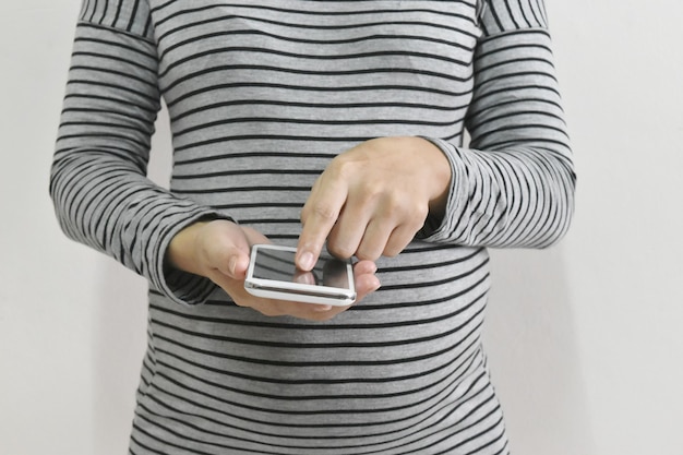 Kobieta w ciąży korzystająca ze smartfona na szarym tle