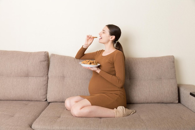 Kobieta w ciąży lubi jeść ciasteczka odpoczywając na kanapie w domu Niezdrowe słodkie ciasto podczas koncepcji ciąży