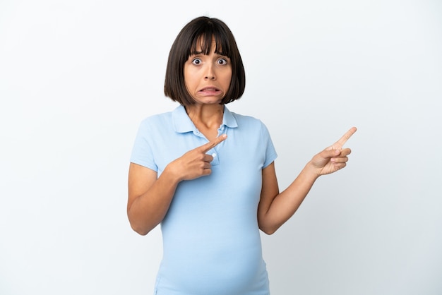 Kobieta w ciąży na białym tle przestraszona i wskazująca na bok