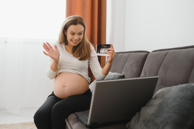 Kobieta w ciąży na czacie wideo z rodziną na laptopie macha ręką do ekranu