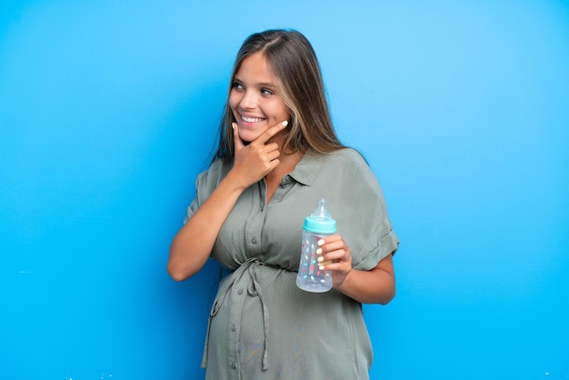 Kobieta w ciąży na niebieskim tle patrząc w bok i uśmiechnięta