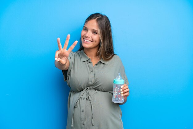 Kobieta w ciąży na niebieskim tle szczęśliwa i licząca trzy palcami
