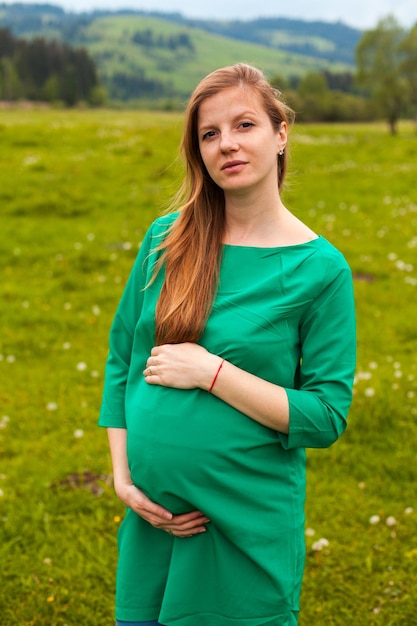 Kobieta W Ciąży O Brązowych Włosach W Zielonej Tunice Oddycha Czystym Powietrzem Na Tle Natury