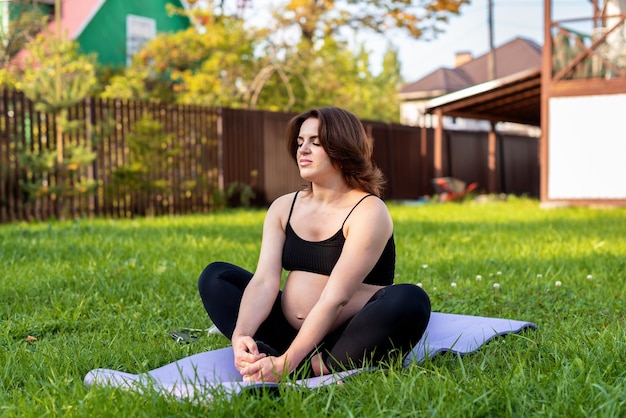 Kobieta w ciąży oddycha i uspokaja się z jogą na świeżym powietrzu wykonując ćwiczenia rozciągające na trawie Samoopieka Yoga w ciąży Koncepcja macierzyństwa Cieszyć się hobby opieki zdrowotnej nad macierzyństwem