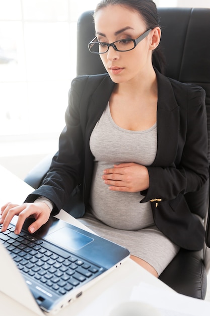 Kobieta W Ciąży. Piękna Kobieta W Ciąży Pracuje Na Laptopie, Siedząc W Swoim Miejscu Pracy W Biurze