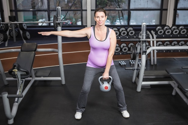 Kobieta w ciąży podnosi kettlebell przy gym