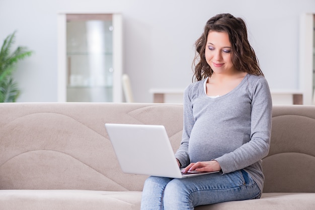 Kobieta w ciąży pracuje na laptopie siedzi na kanapie