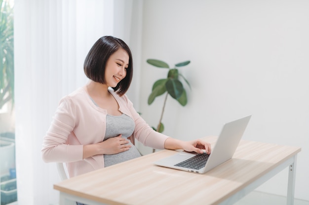 Kobieta w ciąży pracuje na laptopie w domu