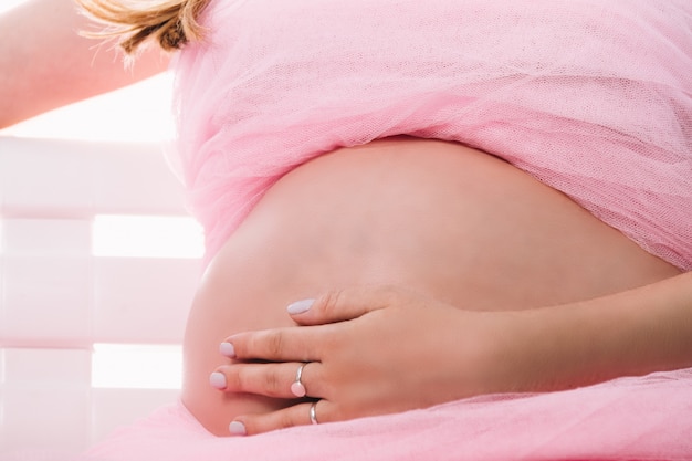 Kobieta w ciąży siedzi dotykając jej brzuch różowymi ubraniami