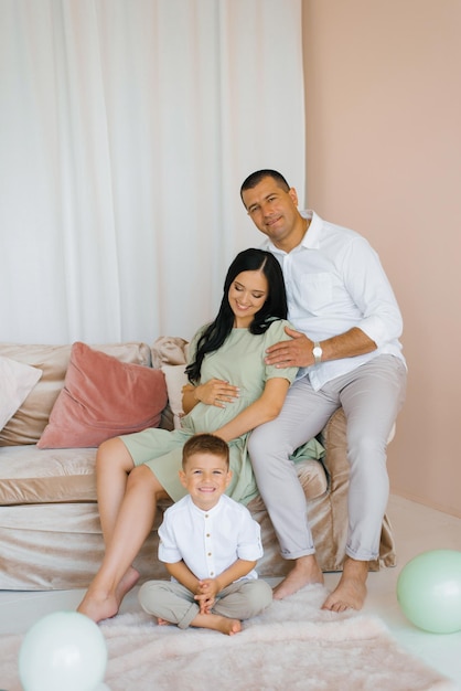 Kobieta w ciąży siedzi na kanapie w otoczeniu męża i syna