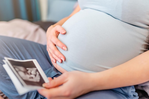 Kobieta w ciąży siedzi na łóżku i ogląda zdjęcia USG dziecka