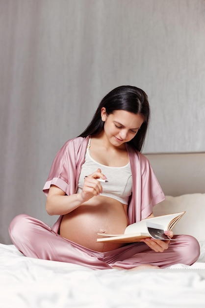 Kobieta W Ciąży Siedzi Na łóżku I Pisze W Zeszycie