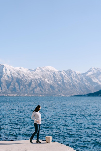 Kobieta w ciąży stoi na molo na tle gór i morza