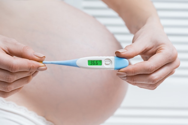 Kobieta w ciąży trzyma elektronicznego termometr z normalną temperaturą. Zdrowie w czasie ciąży.