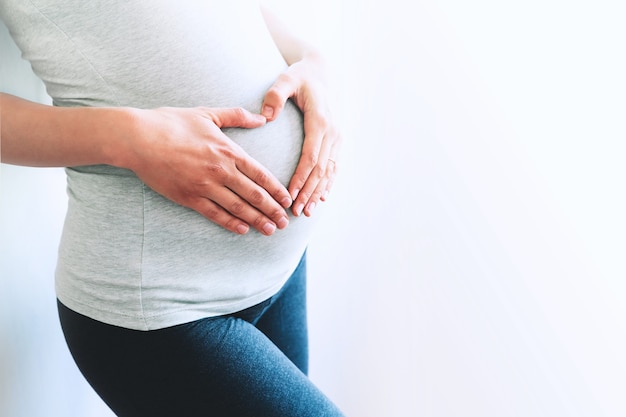 Kobieta w ciąży trzyma ręce na brzuchu w domowych wnętrzach Koncepcja ciąży