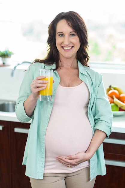 Kobieta w ciąży trzyma sok pomarańczowy w kuchni