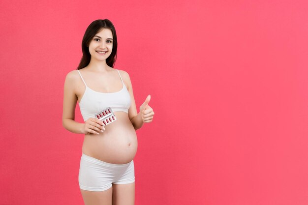 Kobieta w ciąży trzyma stos blistrów tabletek na kolorowym tle z kopią miejsca Witaminy podczas koncepcji ciąży