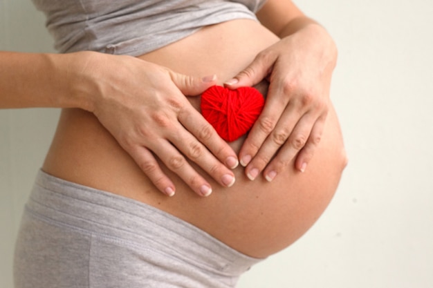 Zdjęcie kobieta w ciąży, trzymając czerwone serce i rękę na brzuchu, symbol nowego życia