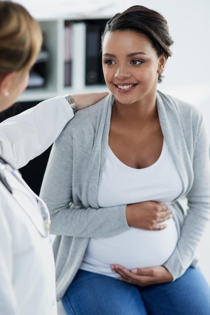 Kobieta w ciąży uśmiecha się i lekarz w szpitalu u dziecka sprawdza ze szczęściem Ciąża żołądka i opieka zdrowotna z profesjonalistą w klinice z afrykańską pacjentką w konsultacji odnowy biologicznej