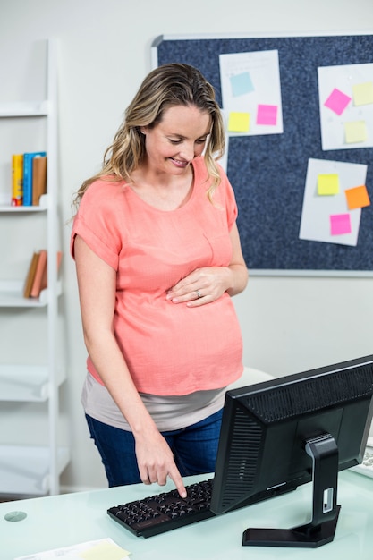 Kobieta w ciąży używa komputer na biurku