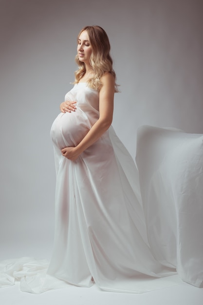 Kobieta w ciąży w białej długiej sukni na jasnym tle