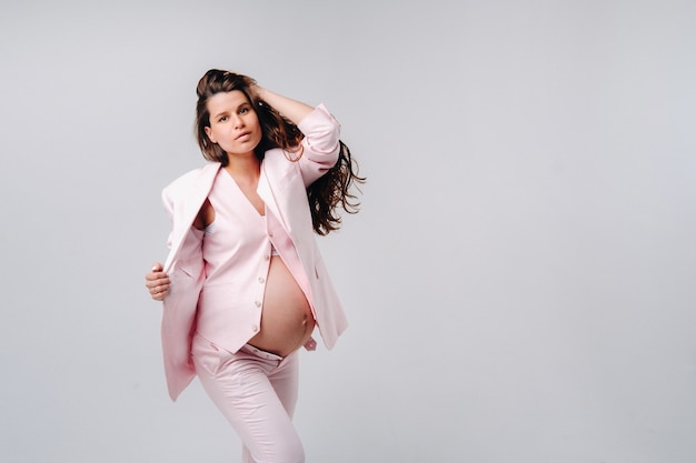 Kobieta w ciąży w różowym garniturze z bliska na szarym tle